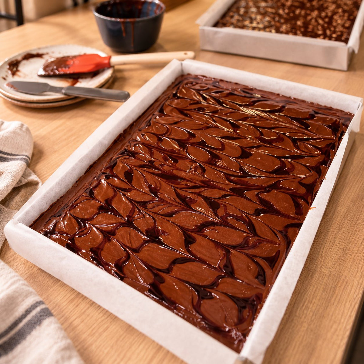 A parchment-lined tray of glossy chocolate brownie batter with a feathered swirl, ready for the oven in the Munchyhub bakery